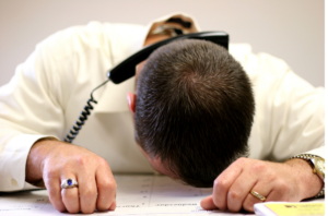 man slumped on desk with phone on his head
