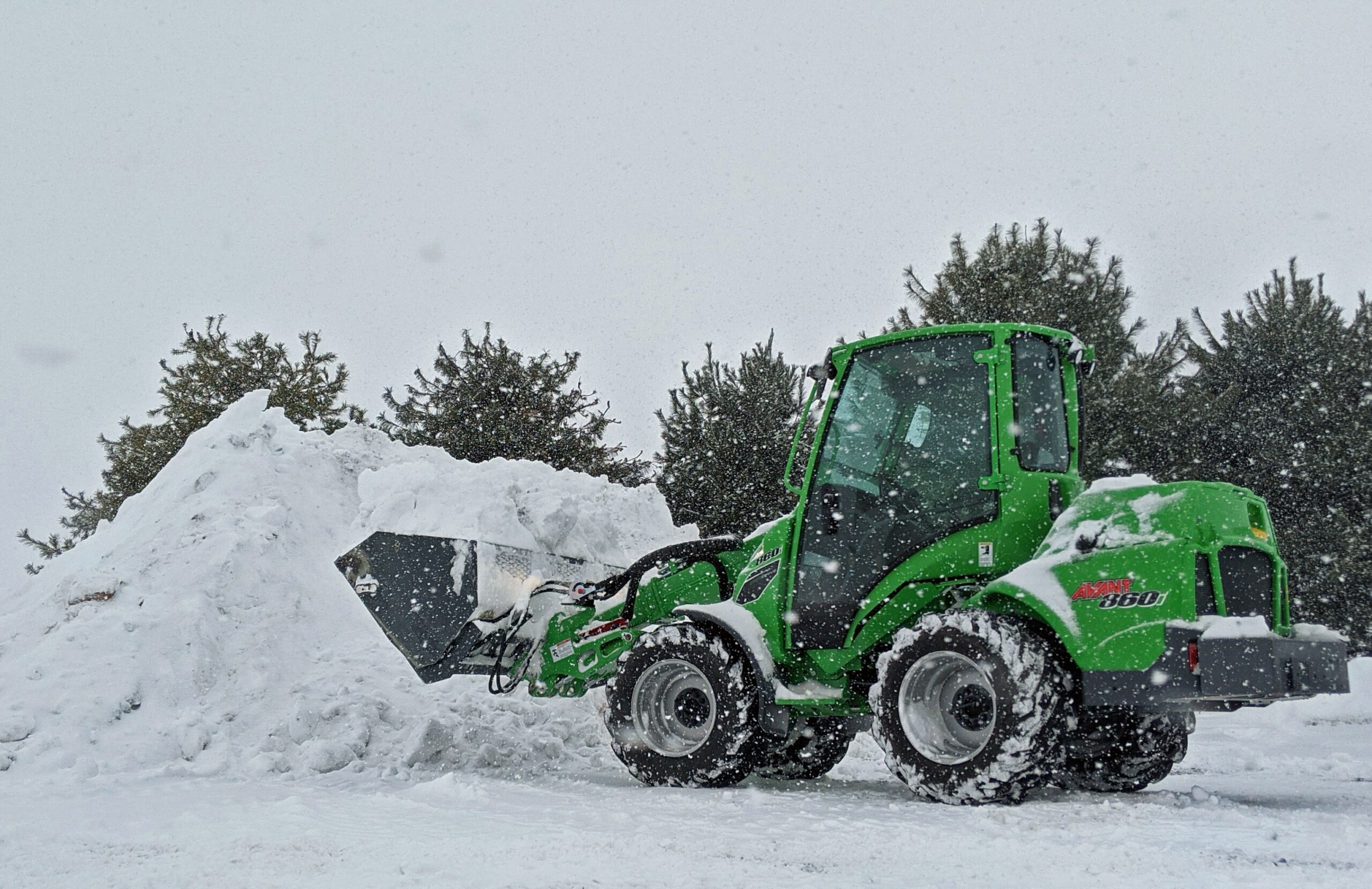 A green snowplow pushes a bunch of snow into a large pile. Even the snowplow business has found a way not to be boring.