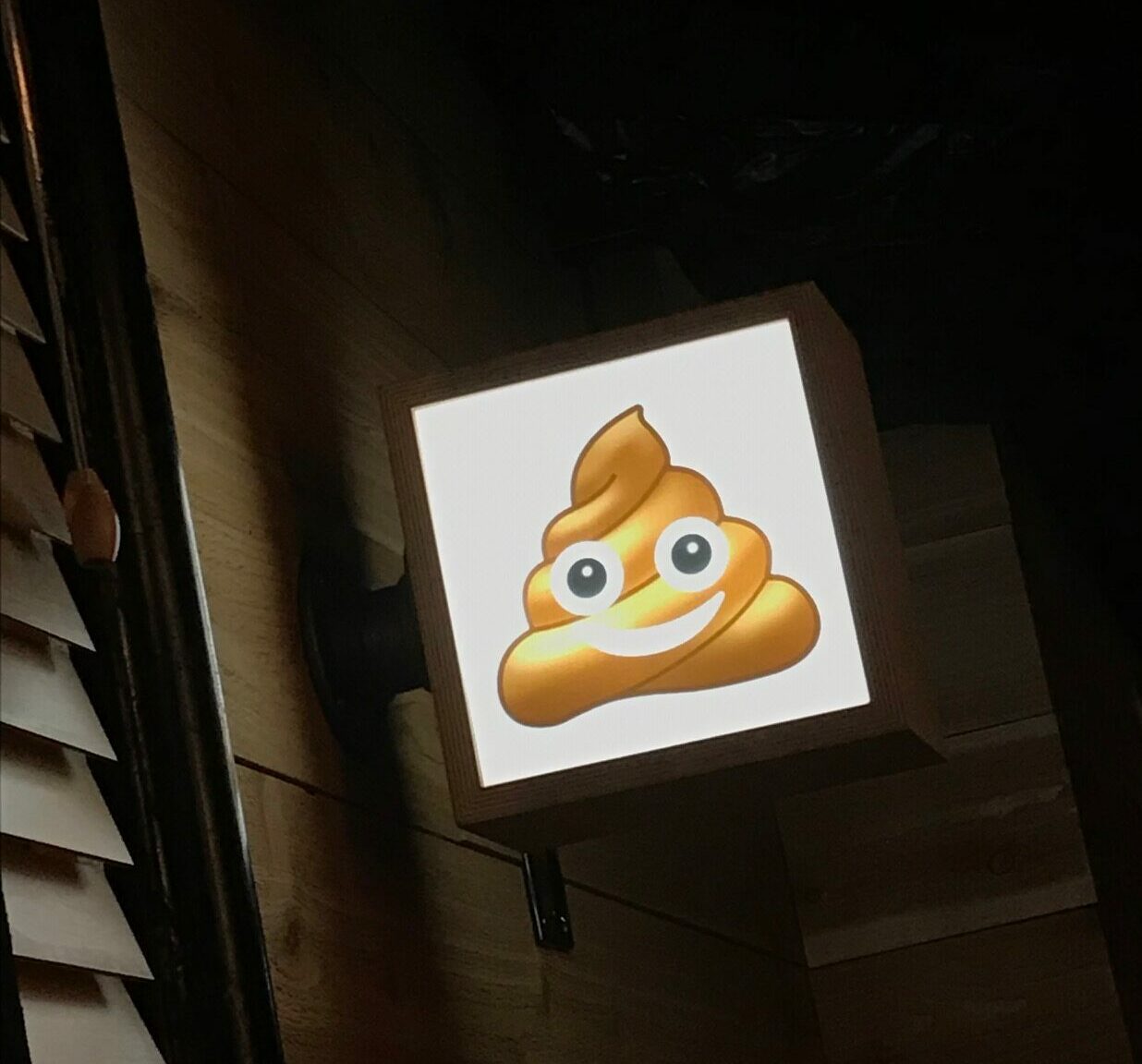 A lit-up "poop emoji" sign shows the way to the bathroom.