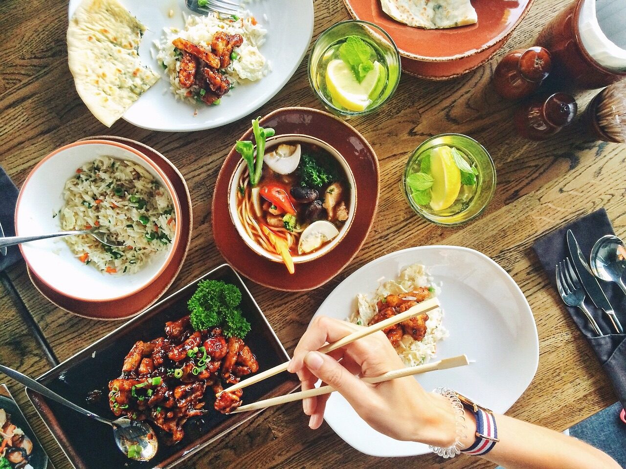 A hand holding chopsticks reaches for a plate of food while other plates adorn the table. Customer experience in the fast casual restaurant industry is about more than just the food.