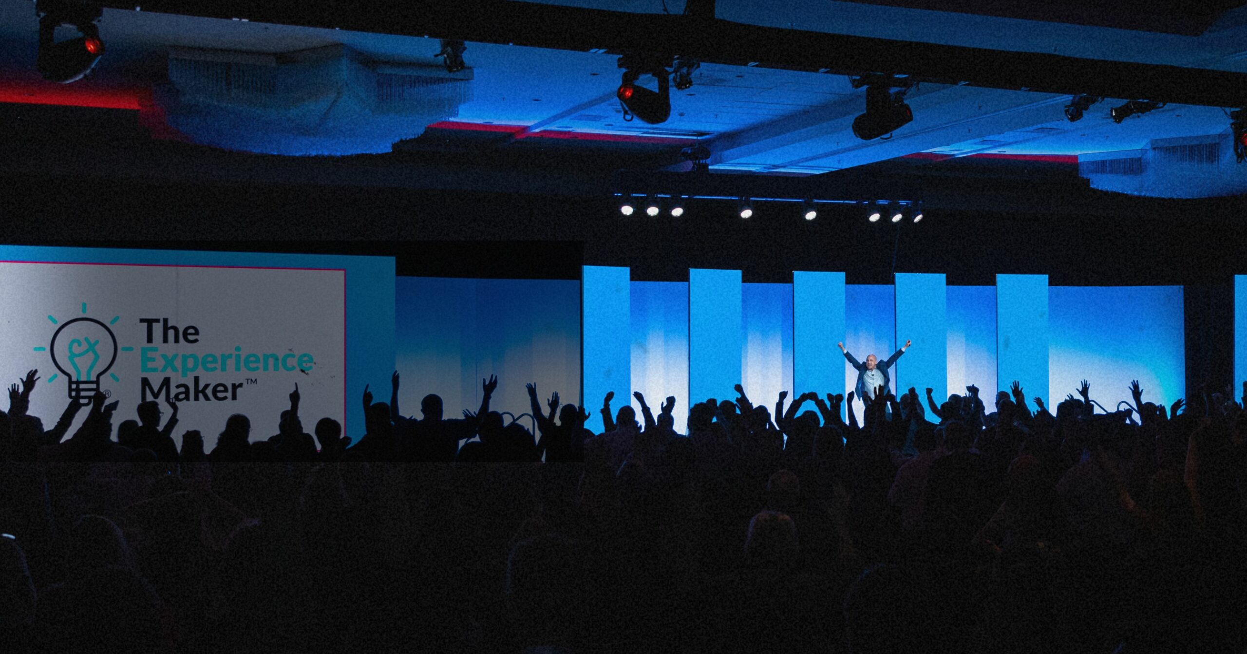 Dan Gingiss, customer experience keynote speaker, on a large stage with his arms up in the air as the entire audience participates with their arms up.