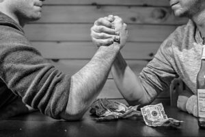 Two arms that are arm wrestling with money on the table. Do you know who your competition is?